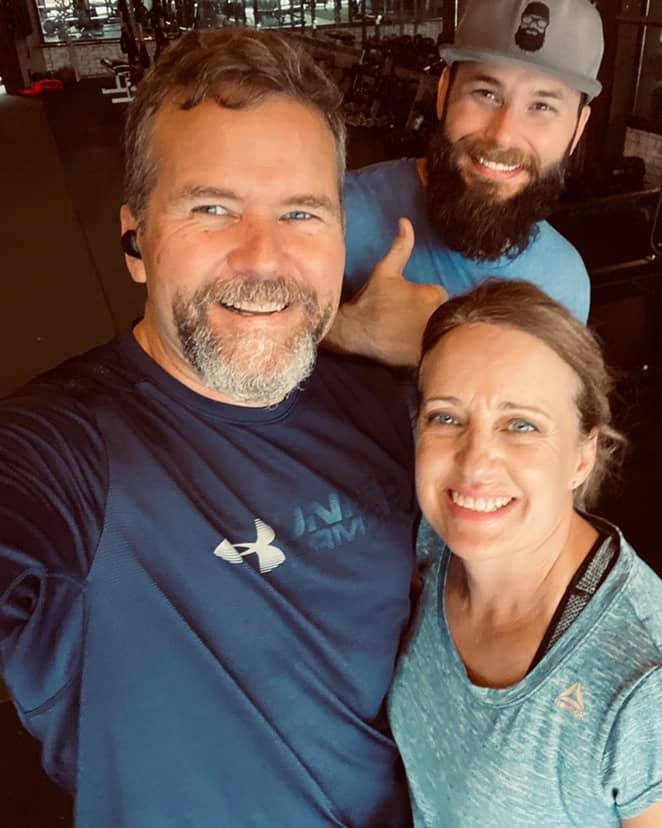 Two adult clients beaming in the gym, their coach behind them
