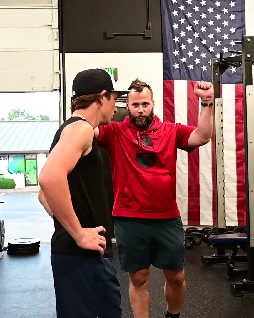 A coach in a red hoodie fist-pumping beside an athlete in the studio